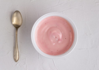 Yoghurt cup with pink strawberry yogurt on grey background with small silver spoon