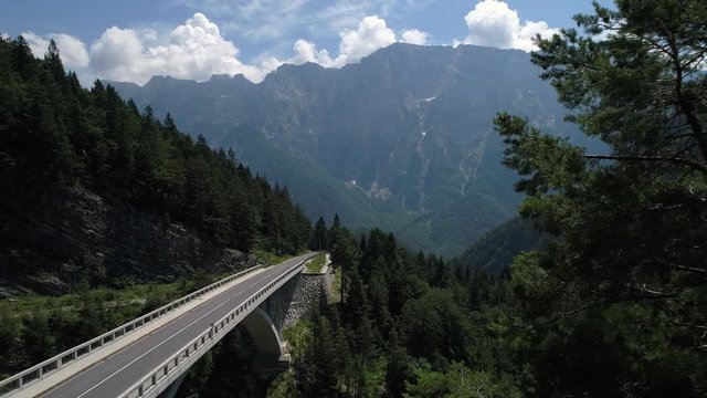Aerial - Longboarding over concrete bridge on mountain pass in spring