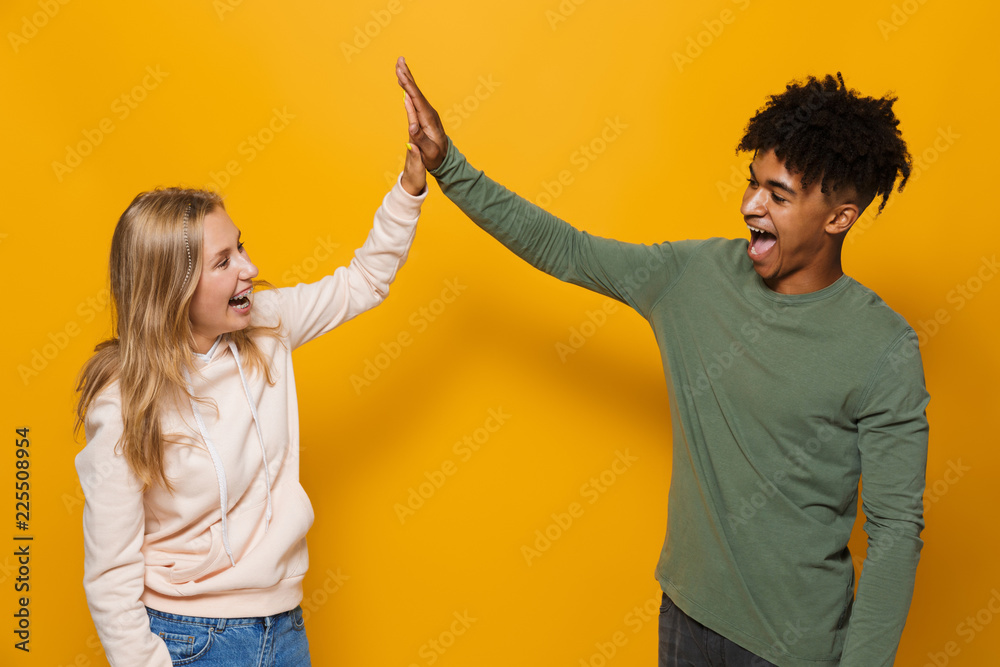 Sticker Photo of adorable students man and woman 16-18 with dental braces laughing and giving high five, isolated over yellow background