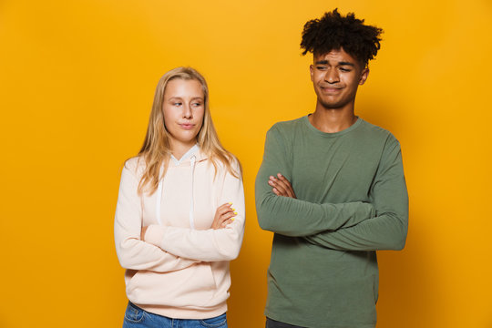 Photo of annoyed students man and woman 16-18 with arms folded after arguing, isolated over yellow background