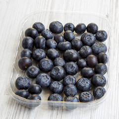 Blueberries in a plastic box over white wooden background, side view. Close-up.
