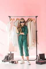 attractive fashionable kid in overalls posing near clothes and footwear in boutique