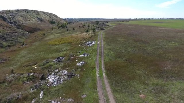Garbage Near Road. Shot by drone. Flight over the dirt road, which has a lot of heaps with garbage. People throw construction garbage, household waste, polluting the environment.