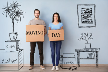 Young couple holding boxes with text MOVING DAY indoors and imagining interior of new house