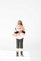 stylish cheerful kid in black suit holding big soft teddy bear on grey