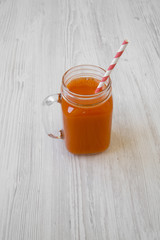 Glass jar of carrot smoothie on white wooden table, low angle view. Close-up.