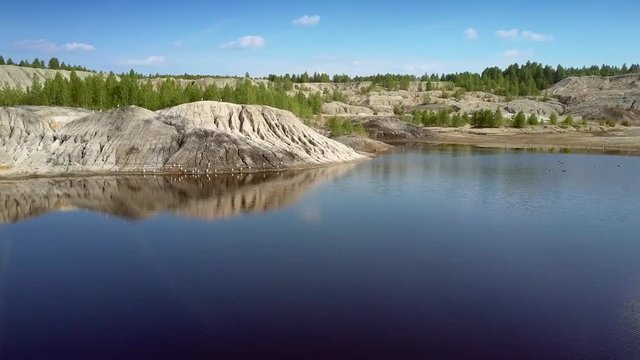 blue lake mirror reflects steep pitted slope under sky
