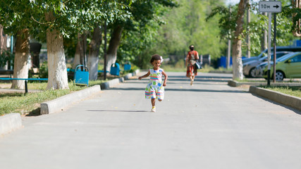 Fototapeta na wymiar Black girl runs on the asphalt. Dark-skinned little girl running along the road in the yard.