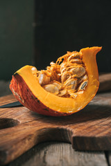 close up view of raw and ripe pumpkin half on cutting board with knife on dark backdrop