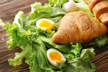 Tasty croissant with boiled egg and lettuce on wooden table
