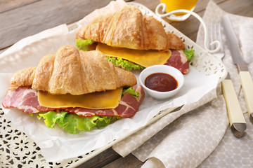 Tasty croissant sandwiches with sauce on tray