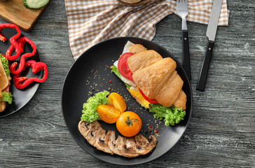 Tasty croissant sandwich with vegetables on plate