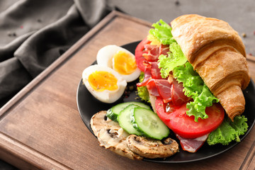 Plate with tasty croissant sandwich on wooden board