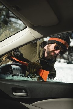 Man cleaning snow from car windshield