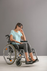 Naklejka na ściany i meble Depressed young woman in wheelchair against grey wall