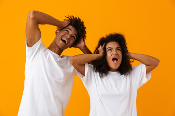 Screaming emotional young cute african couple posing isolated over yellow background.