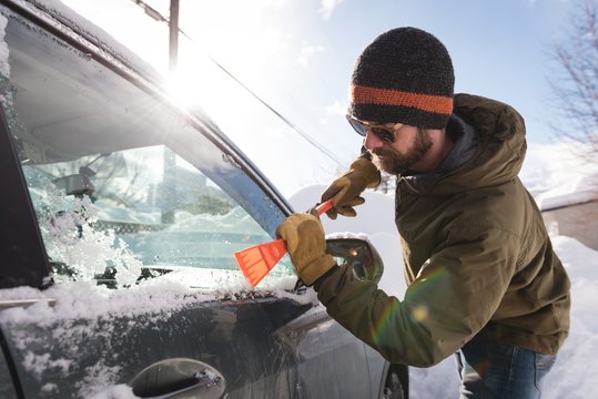 Man cleaning snow from car windshield