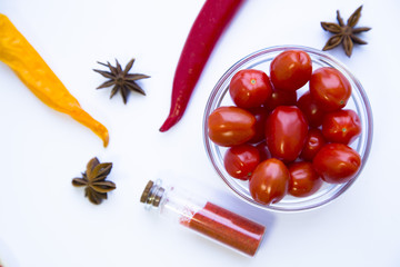 Dry spices and herbs in glass jar with a cork, a bowl of cherry tomatoes and chili peppers, white background