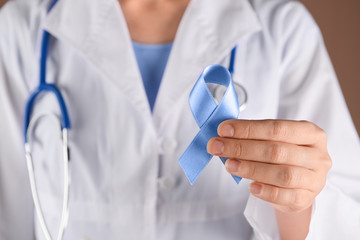 Female doctor holding blue ribbon, closeup. Prostate cancer awareness concept