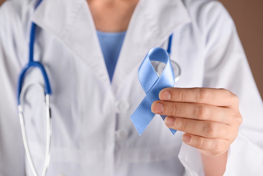 Female doctor holding blue ribbon, closeup. Prostate cancer awareness concept - Powered by Adobe