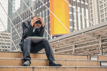 Desperate asian businessman with hands on head sitting on concrete stairs in urban city area. Emotional pain, sadness, business problems and depression concept