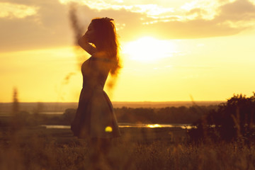 silhouette of a dreamy girl in a field at sunset, a young woman enjoying nature