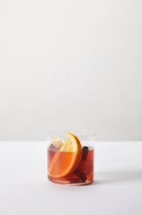 close up view of hot mulled wine in glass with orange pieces on white tabletop on grey background