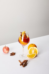 close up view of mulled wine in glass and ingredients arranged around on white tabletop on grey...