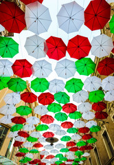 Fototapeta na wymiar A lot of red white and green umbrellas hanging above the street