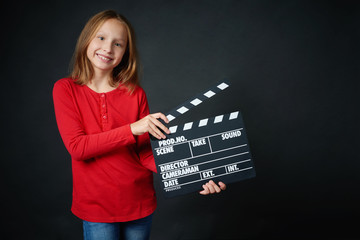 Happy smiling girl holding clap board, over dark background