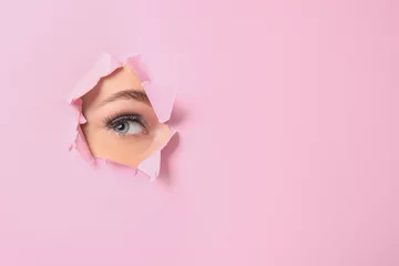 Foto op Plexiglas Eye of beautiful young woman visible through hole in pink teared paper © Pixel-Shot