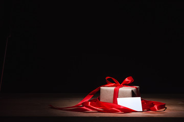 craft gift box tied with red ribbon and decorated with small glitter paper on wooden table, white...