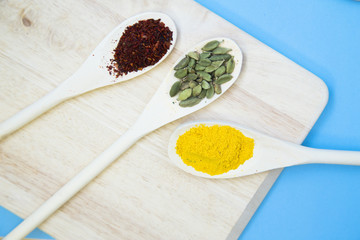 Dry spices, beans and herbs in wooden spoons on a wooden cutting board, light blue background
