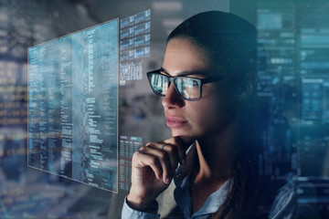 Close up of a beautiful girl with glasses while she is working with a futuristic computer with holograms. Concept: Future, technology, work - obrazy, fototapety, plakaty