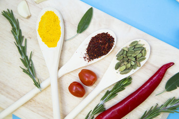 Dry spices, beans and herbs in wooden spoons on a wooden cutting board, light blue background