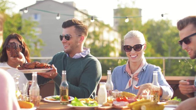 leisure and people concept - happy friends eating and drinking at rooftop party in summer