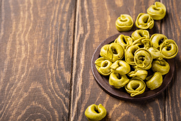 Homemade Tortellini with spinach, cheese and ricotta on wooden board. Healthy italian food concept with copy space.