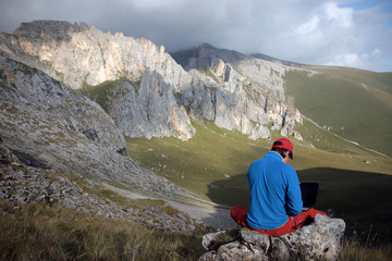 Fototapeta premium A man works on a laptop sitting on top of a mountain.