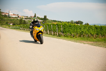 Fototapeta premium Man drive a motorbike on a country road with vineyards in background