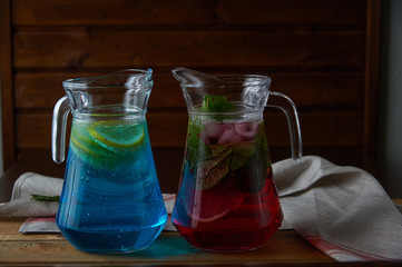 Two glass decanters, carafes, flagons with orange and berry lemonde on a wooden table with a black background