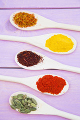 Cooking Hot Spicy Food Concept. Dry spices,beans and herbs in plastic cup, glass jar with cork and wooden spoon, purple wooden background