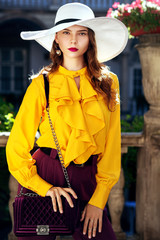 Outdoor fashion portrait of young beautiful woman wearing stylish white hat, yellow blouse with...