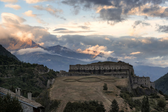 Dramatic view at Exilles Fort with high cloudy mountains on the background