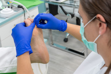 Female chiropodist, attending elder in a clinic and performing podiatric treatments