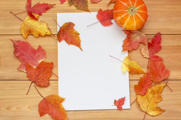 Autumn leaf composition. Blank paper sheet with orange leaves and pumpkin on wooden background....