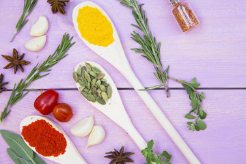 Cooking Hot Spicy Food Concept. Dry spices,beans and herbs in plastic cup, glass jar with cork and wooden spoon, purple wooden background