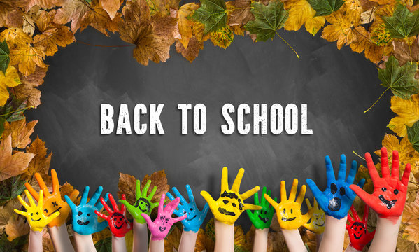in bunten Farben angemalte Kinderhände und Kreidetafel mit Aufschrift "Back to school" und Herbslaubumrandung