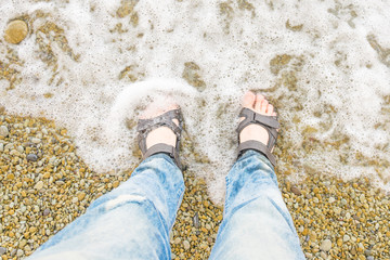 Male feet in sandals in the water at the beach.