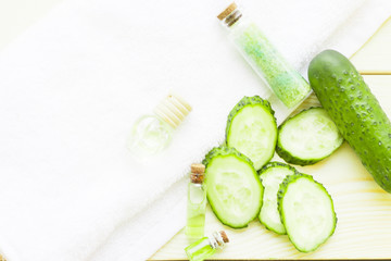 Cucumber home spa and hair care concept. Sliced cucumber, bottles of oil, jar of mask, bathroom towel. White board background