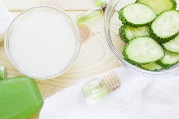 Cucumber home spa and hair care concept. Sliced cucumber, bottles of oil, soap, jar of mask, bathroom towel. White board background
